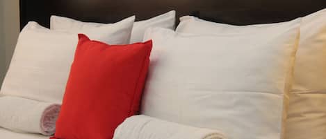Un lit avec des oreillers blancs et rouges, une serviette enroulée et une tête de lit sombre.