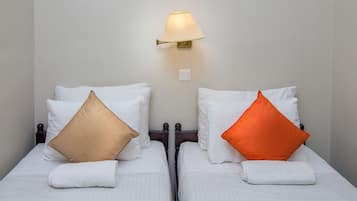 Two single beds with white linens, each with a pillow and a rolled white towel. A wall-mounted lamp is above the beds.