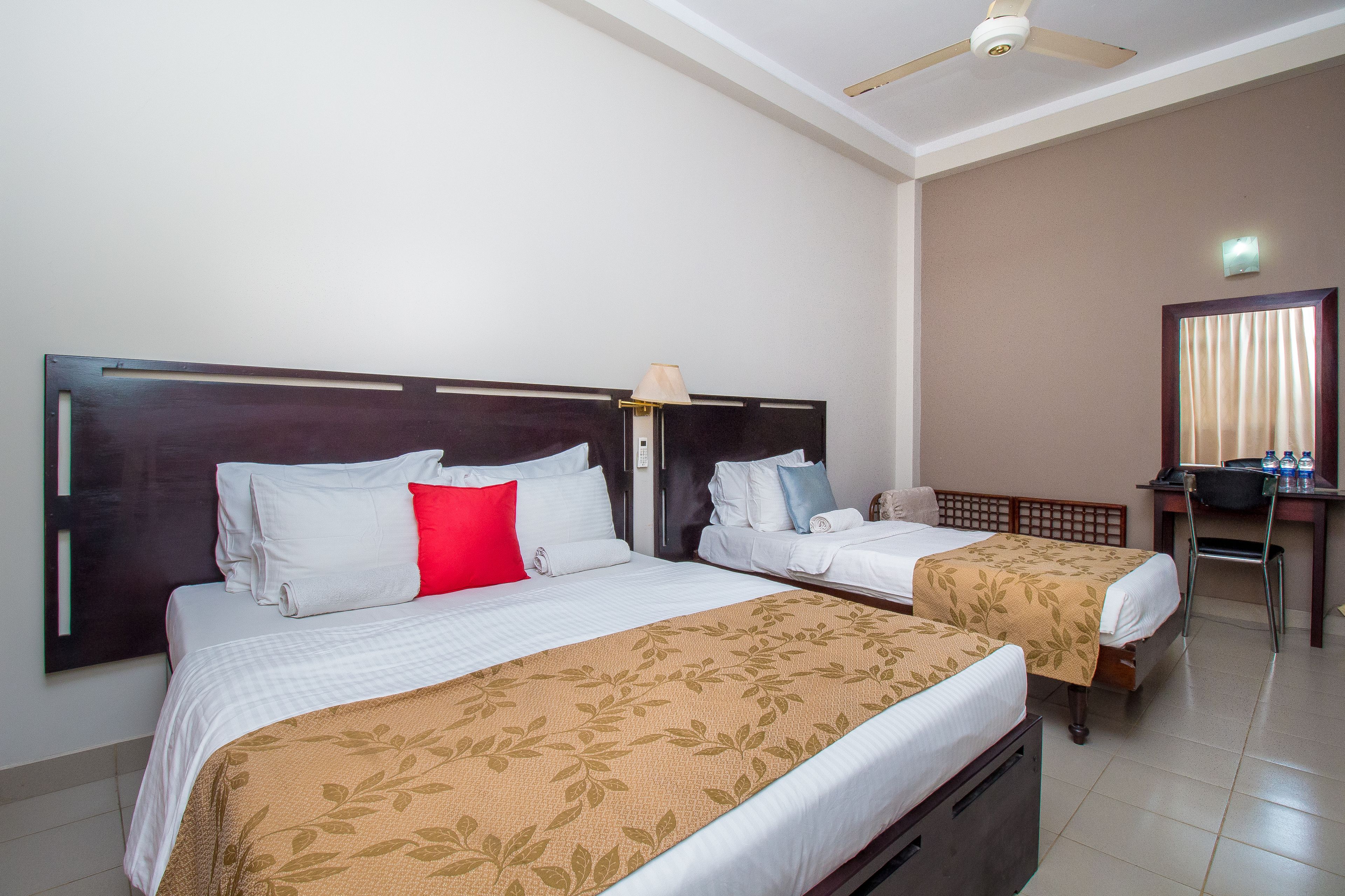 A hotel room with two beds, a desk, and a ceiling fan.