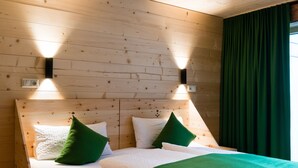 A wooden-paneled room with a bed, green pillows, and wall-mounted lighting.