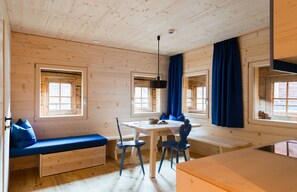 A wooden cabin interior with a dining table, chairs, a bench, and large windows.