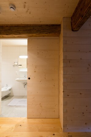 A wooden interior with a door leading to a bathroom featuring a sink and mirror. - Ferienwohnungen am Berg - Giatla Haus (Innervillgraten)
