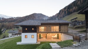 A two-story wooden house with a balcony, set in a mountainous area.