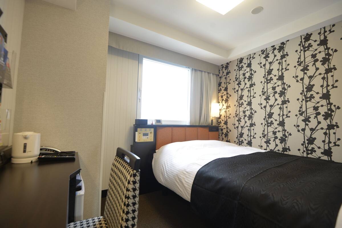 A hotel room with a bed, a desk with a telephone, a coffee maker, and a chair.