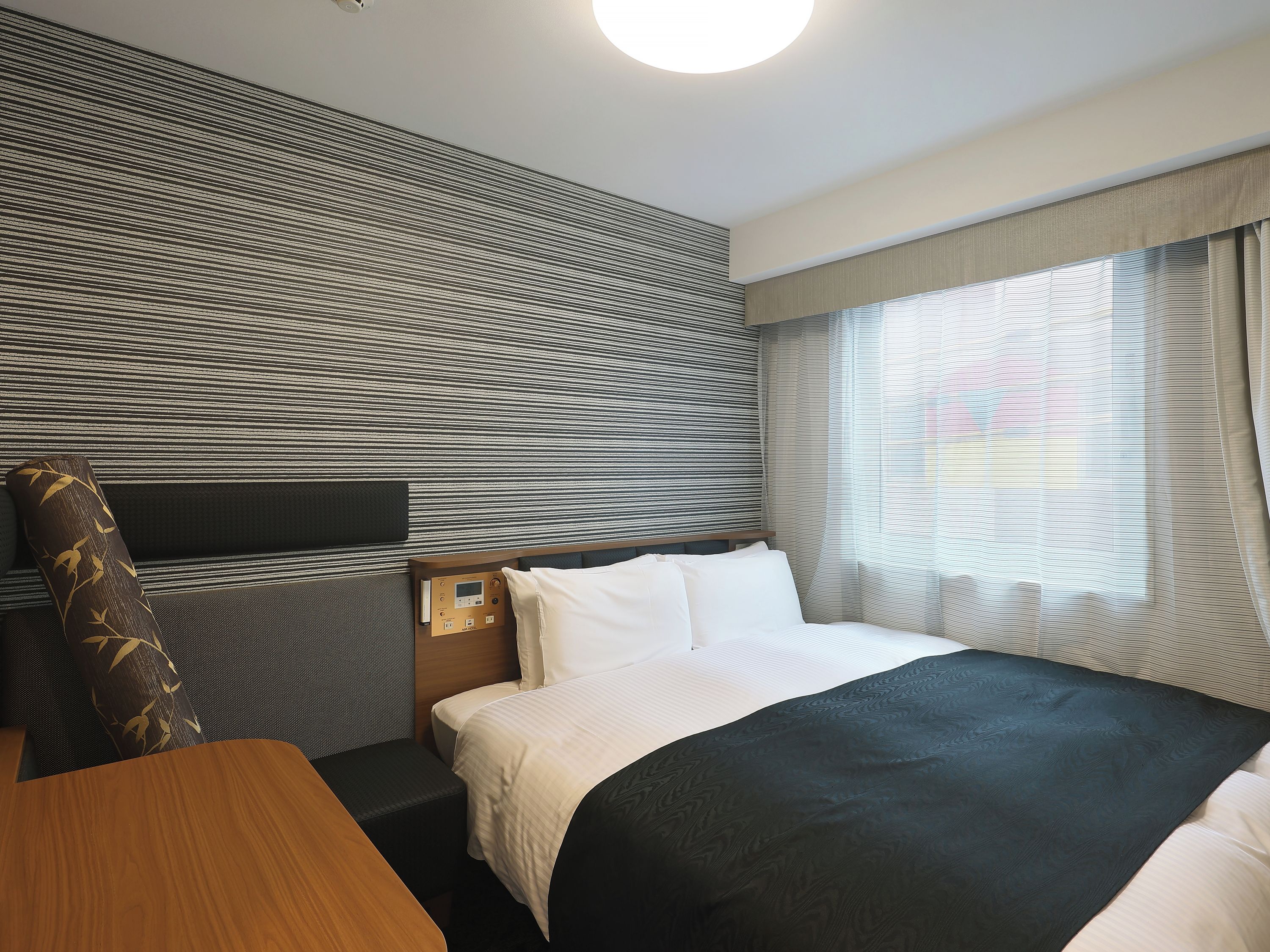 A hotel room with a bed, bedside table, and a headboard with a control panel.