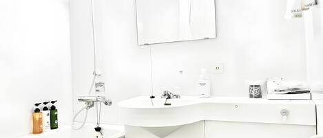 A modern bathroom with a white sink, mirror, and toilet. There are toiletries on the counter and a showerhead above the sink.