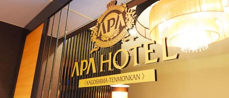 Un letrero de APA HOTEL con una araña y persianas verticales al fondo.
