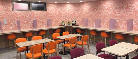 Un salón de conferencias con mesas y sillas, papel tapiz con motivos florales e iluminación en el techo.