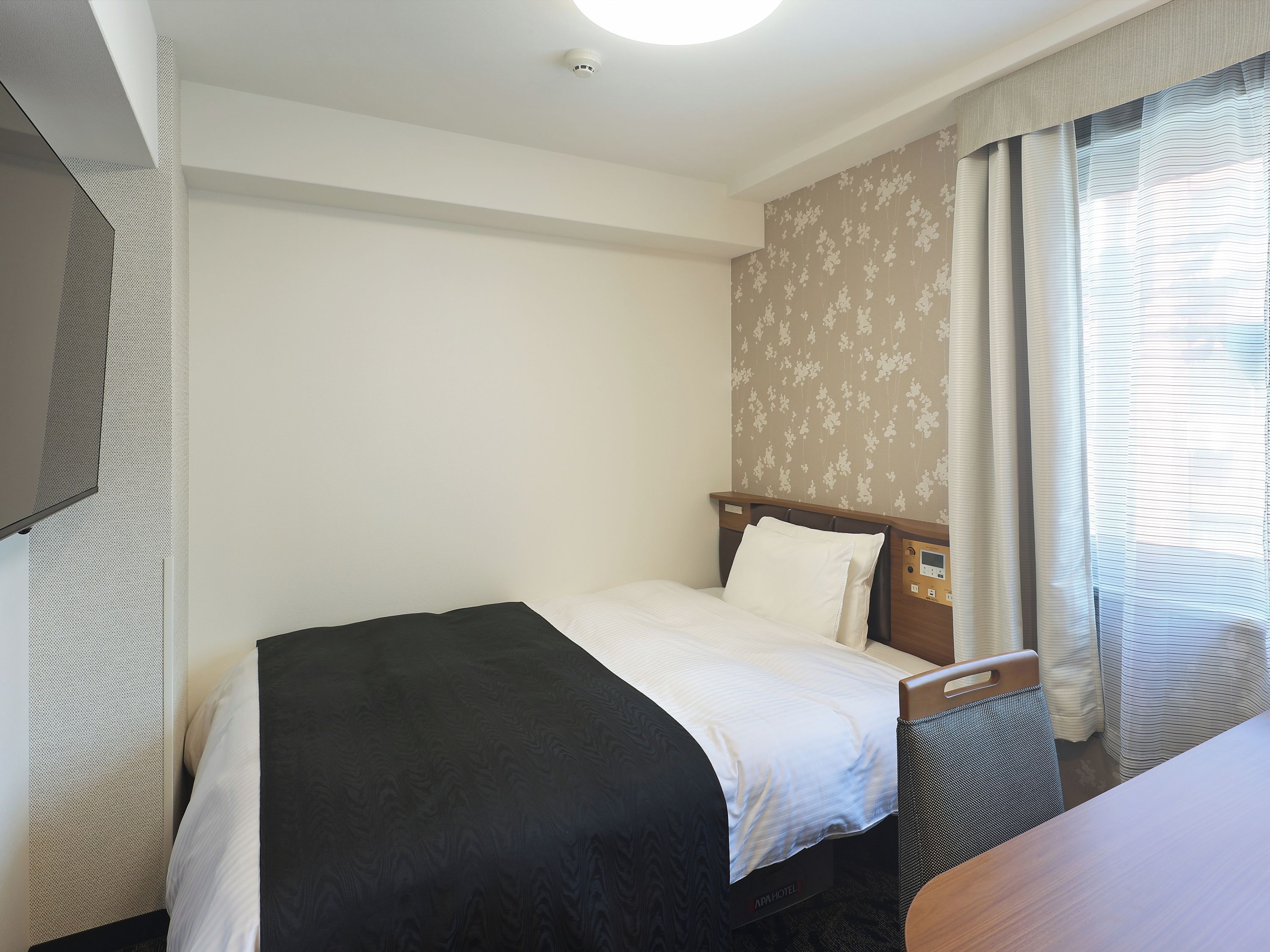 A hotel room with a bed, a desk, and a television on the wall.