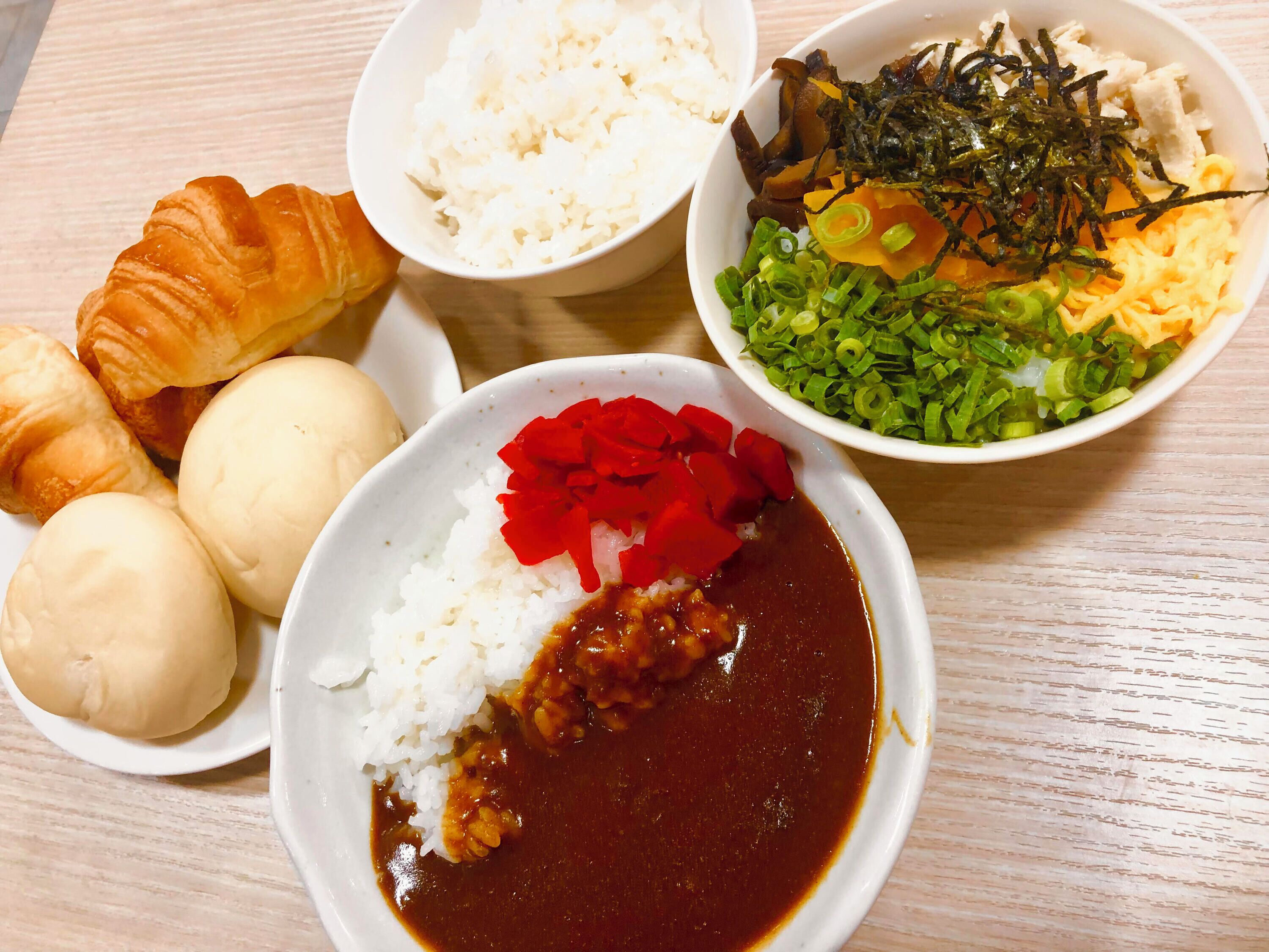 Una mesa con diversos alimentos, incluyendo arroz, un tazón de sopa, una rebanada de pan y un plato con verduras y algas marinas.