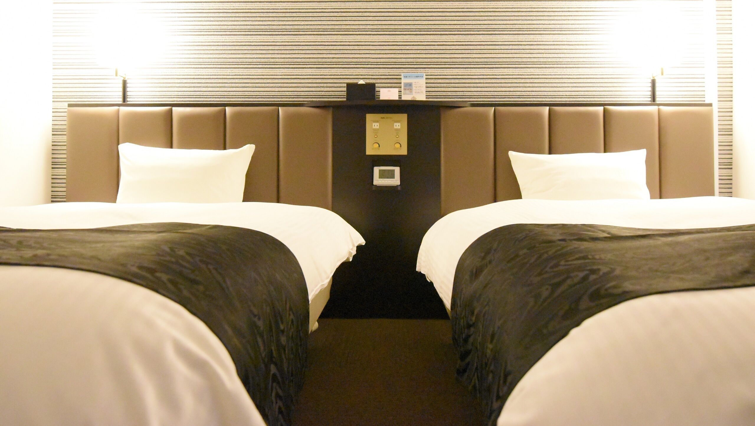 Habitación de hotel con dos camas, cabecera con panel de control y ventana con persianas.