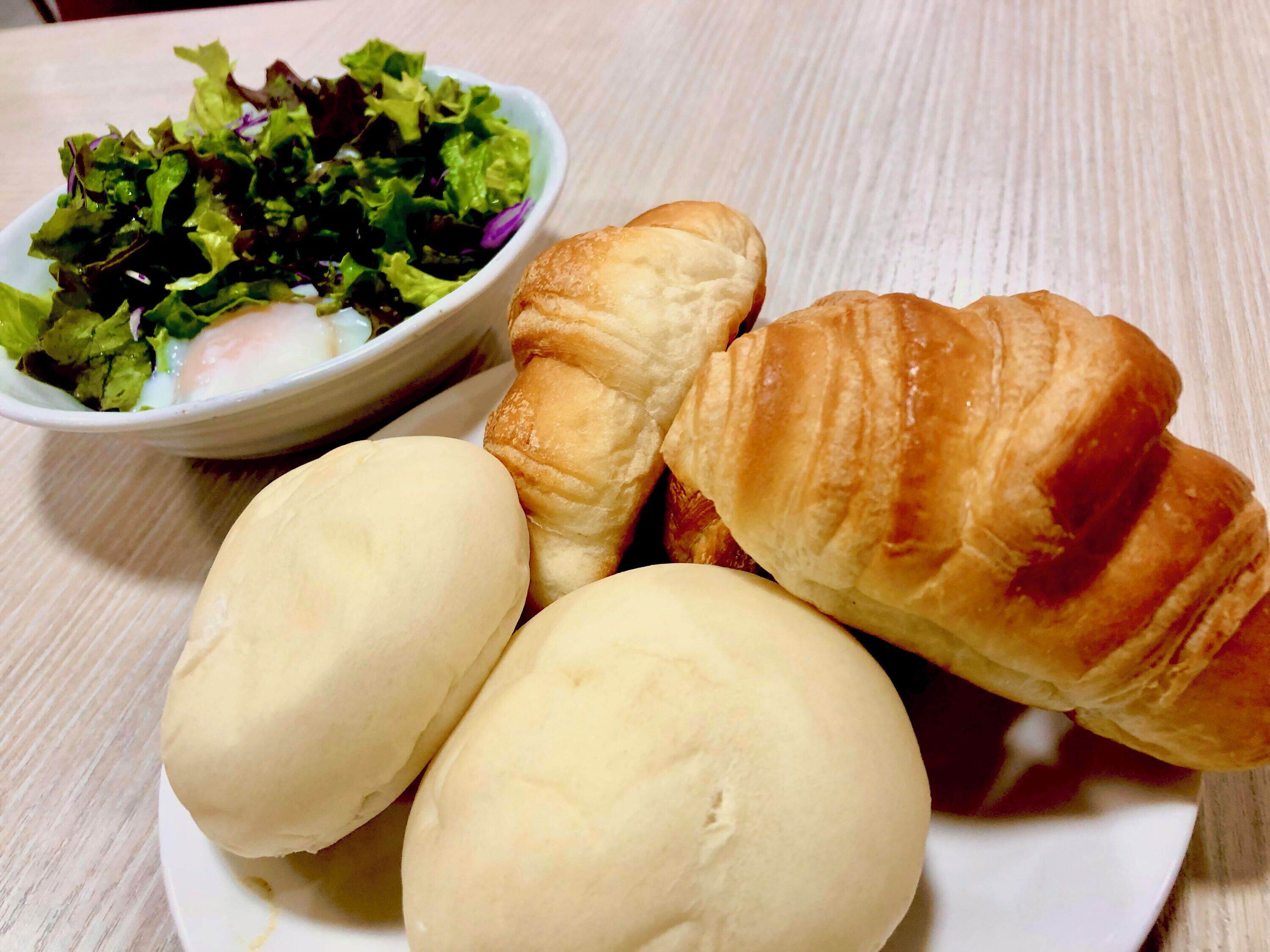 A plate with three buns and a croissant, and a bowl of salad.