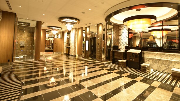 A hotel lobby with a checkered floor, marble columns, and a reception area with a counter and seating. - APA Hotel Kagoshima Tenmonkan (Kagoshima)