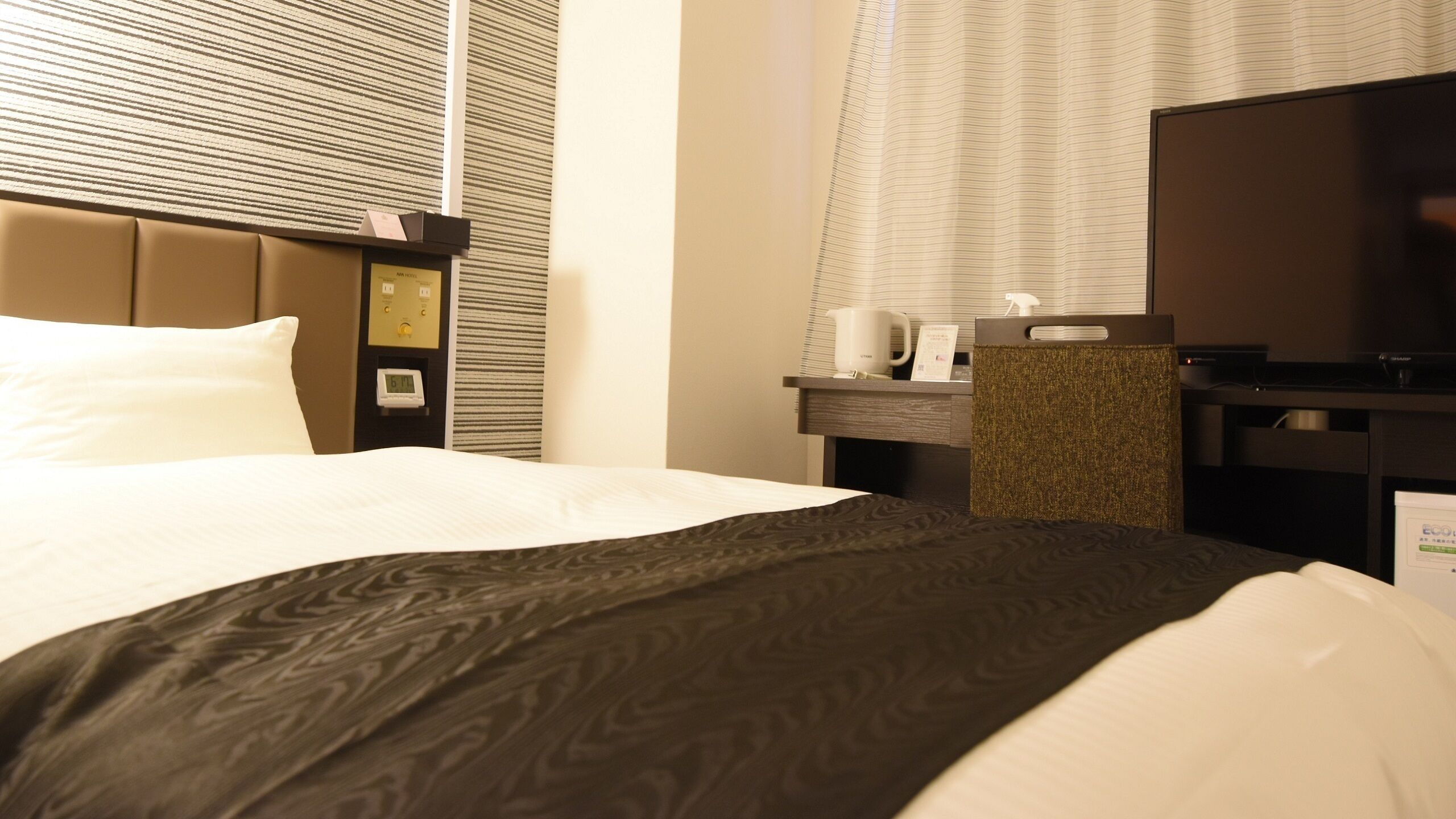 Una habitación de hotel con cama, escritorio, televisión y ventana con persianas.