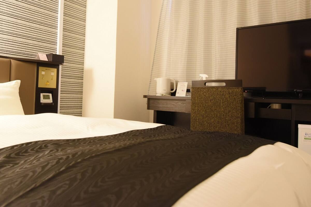 A hotel room with a bed, a desk, a television, and a window with blinds.