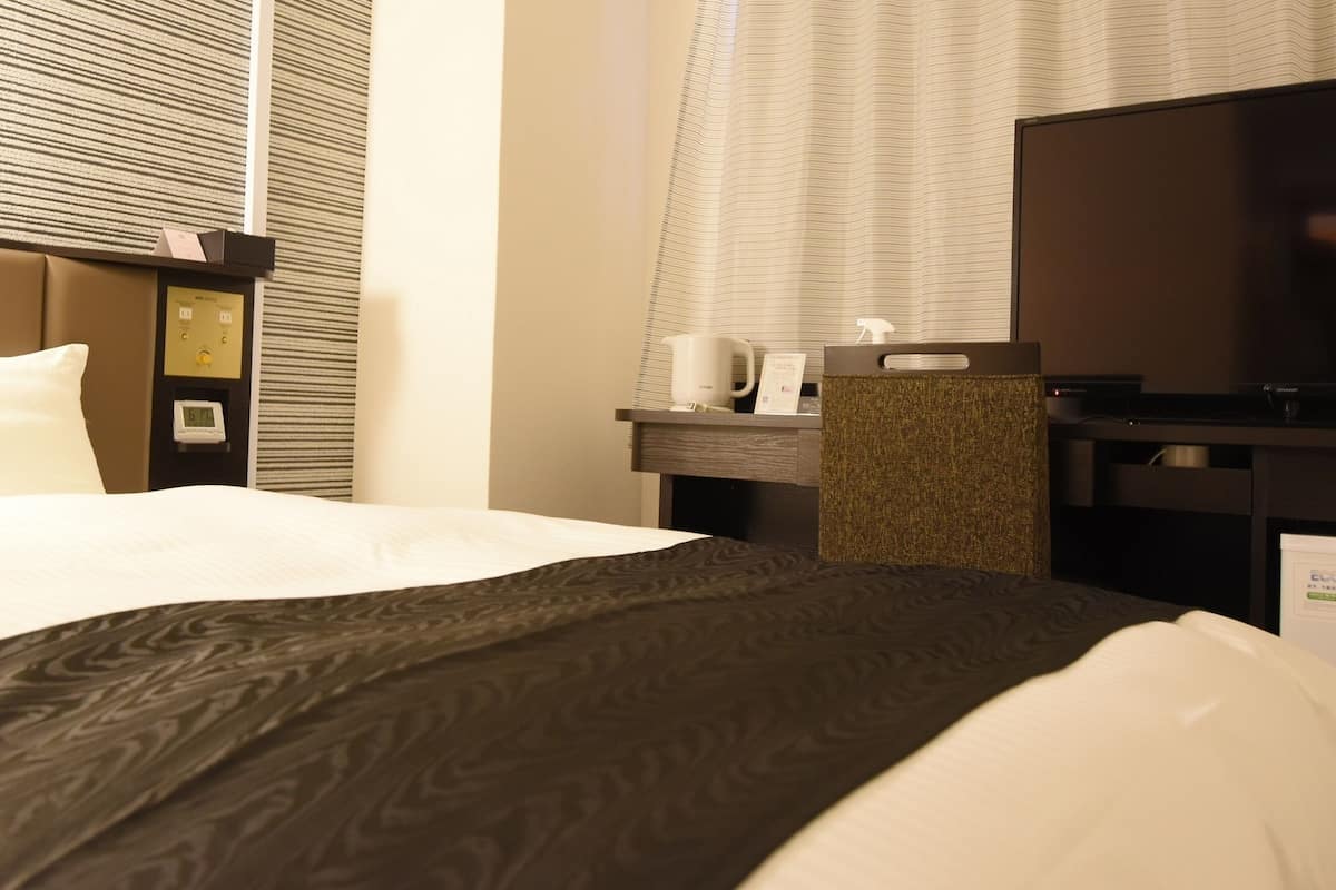 A hotel room with a bed, a desk, a television, and a window with blinds.