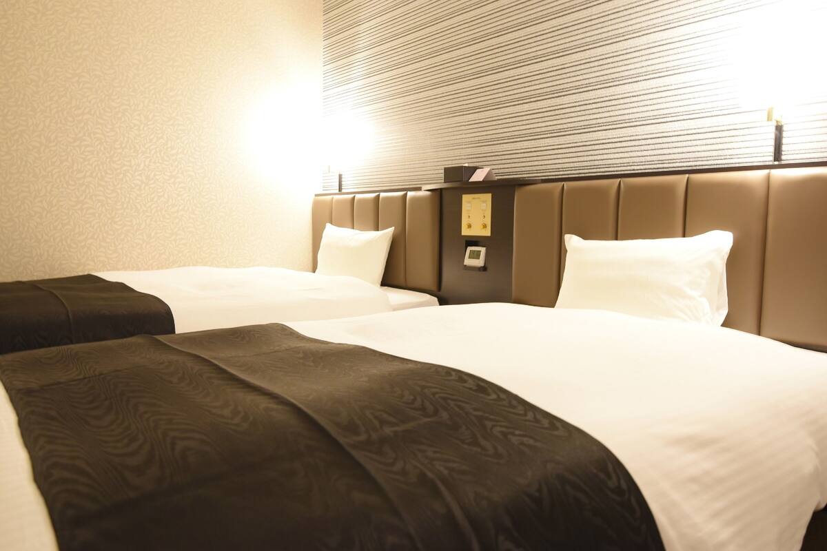 A hotel room with two beds, a headboard with a control panel, and a patterned wall.
