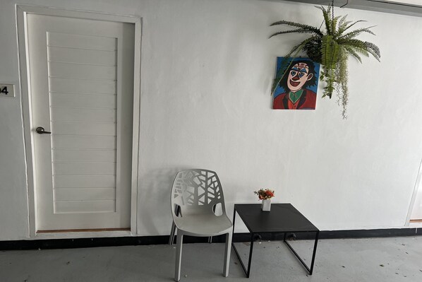 A room with a white door, a white chair, a small black table with a vase, and a painting on the wall. - The Season Airport Udonthani (Udon Thani)