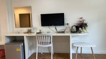 A compact hotel room with a small kitchenette, a desk with a flat-screen TV, a white chair, and a small refrigerator.