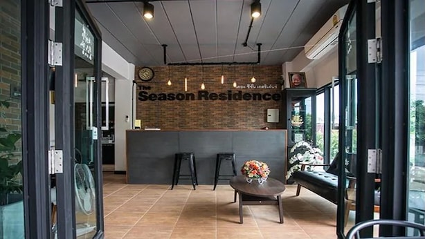 Un espace d’accueil avec un mur en briques, un comptoir d’accueil, deux tabourets de bar, une table ronde ornée d’un vase de fleurs et de grandes fenêtres.