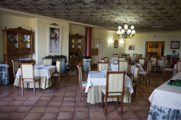 Un comedor con varias mesas y sillas, armarios de madera con cristalería, y un candelabro.