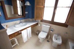 Un baño con lavamanos doble, inodoro, bidé y un espejo con lámpara.