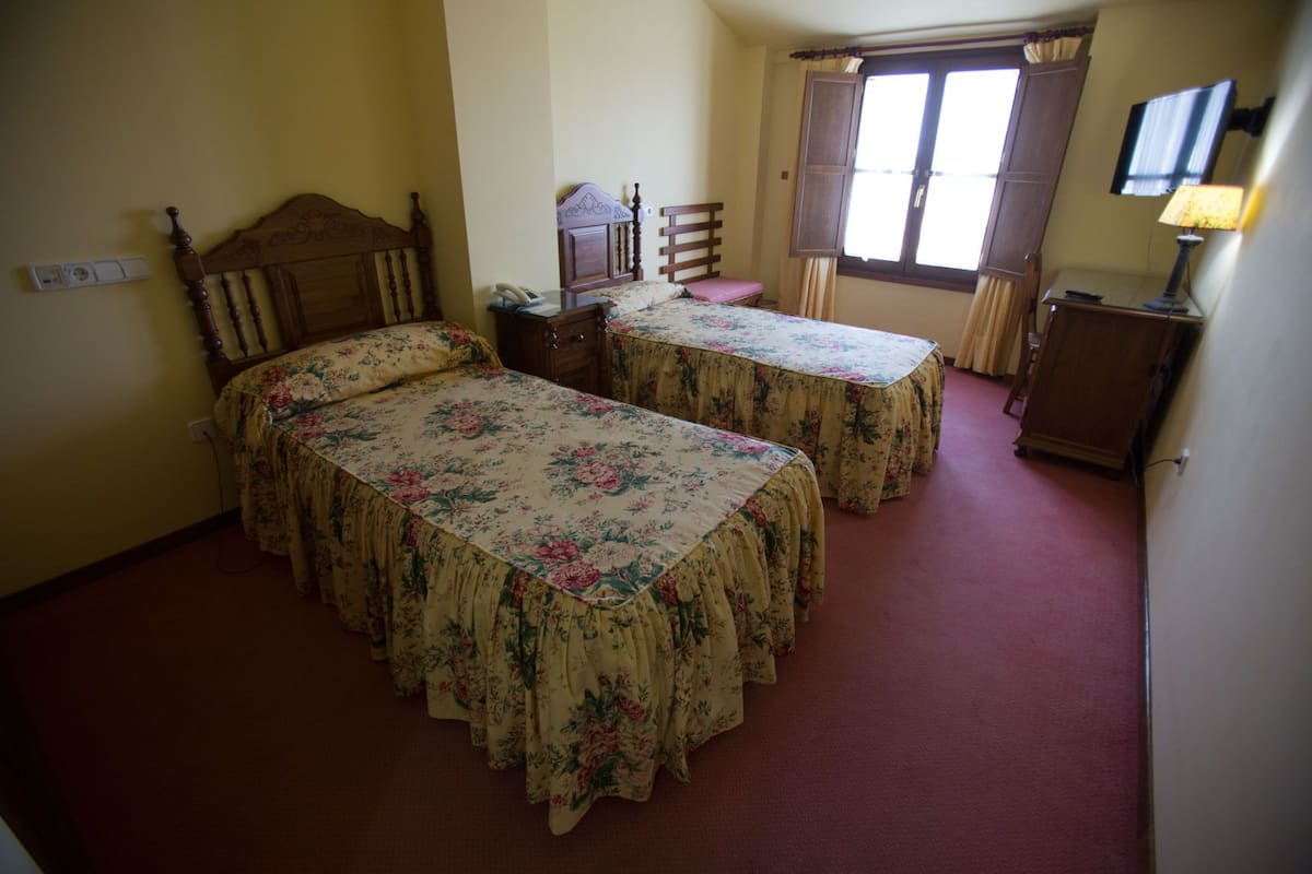 Une chambre avec deux lits, un bureau, une chaise, une télévision et une fenêtre avec des rideaux.