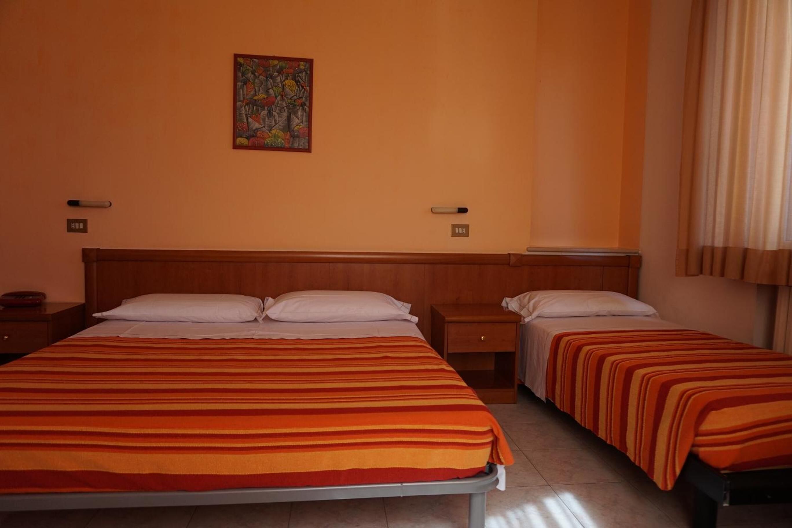 Ein Hotelzimmer mit zwei Betten, einem Holzkopfbrett, einem Bild an der Wand und einem Fenster mit Vorhängen.