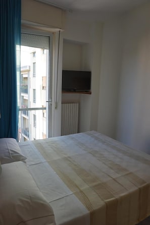 Une chambre d’hôtel avec un lit, un téléviseur fixé au mur et une fenêtre avec des rideaux.