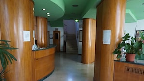 A reception area with wooden reception desks, a staircase, and a potted plant. - Hotel San Marco (Pesaro)