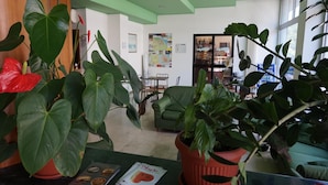 A reception area with a green ceiling, potted plants, a counter with brochures, and a seating area with a green sofa and chairs. - Hotel San Marco (Pesaro)