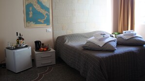 Een hotelkamer met een bed, een klein bureau met een koffiezetapparaat, een kaart aan de muur en een raam met gordijnen.
