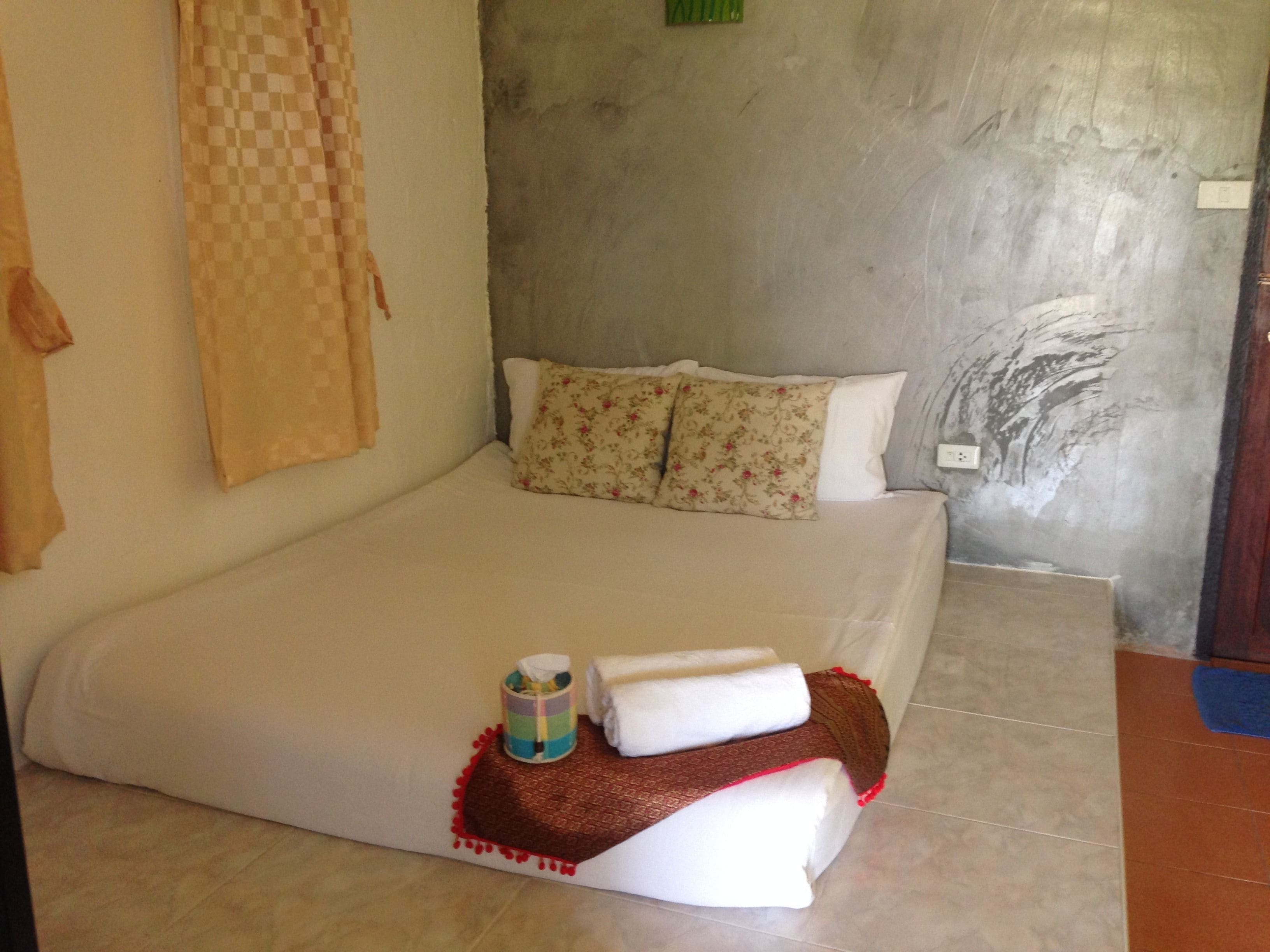 A bedroom with a bed, pillows, a blanket, and a small table with a cup and a tissue.