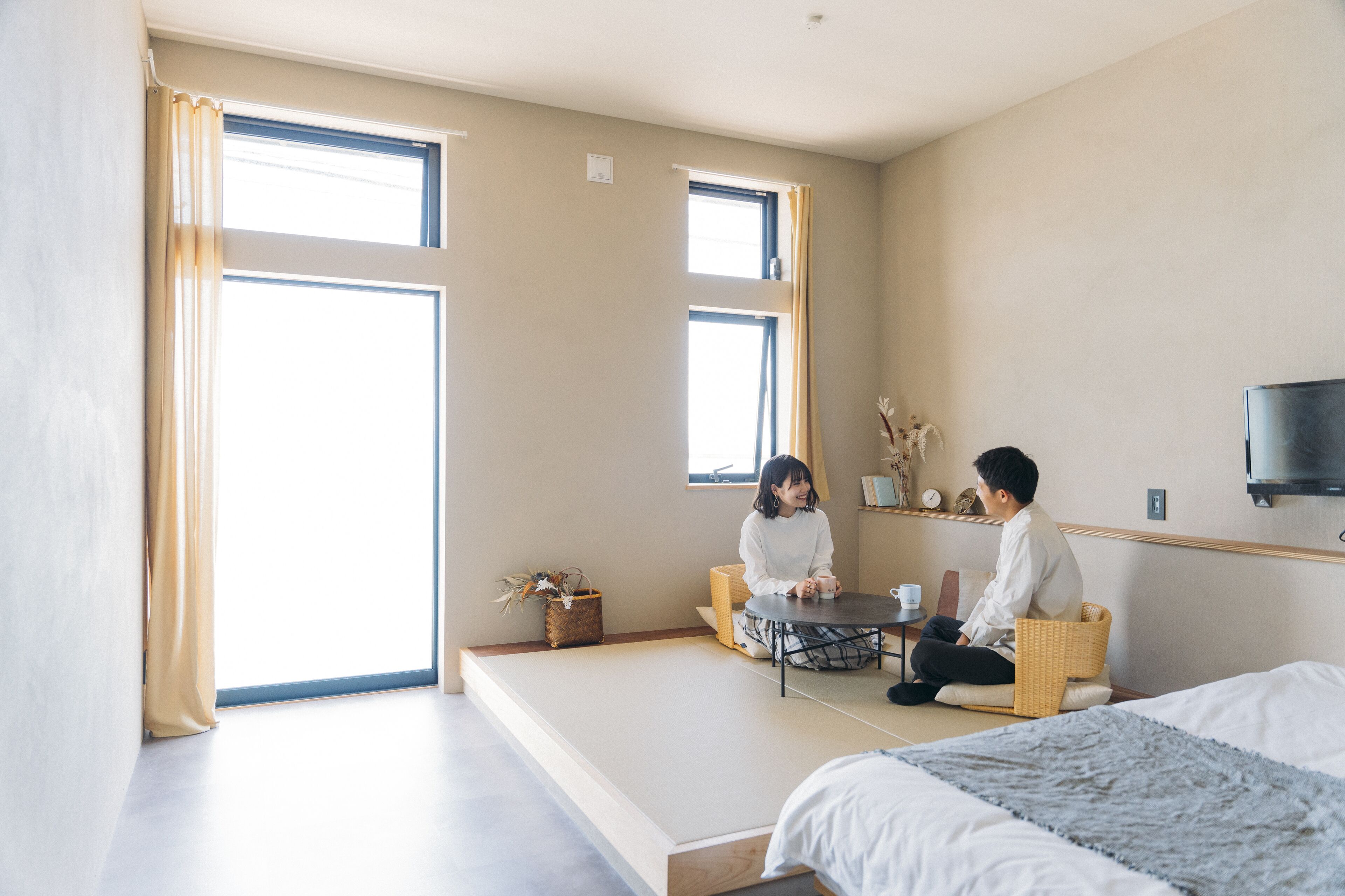 Una habitación con suelo de tatami, una mesa baja y una cama con edredón blanco.
