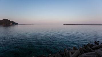 Mar en calma con aguas cristalinas, un rompeolas rocoso y una isla en la distancia.