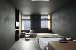 Une chambre d’hôtel moderne dotée d’un grand lit, d’un petit coin salon et offrant une vue sur la mer grâce à de grandes fenêtres.