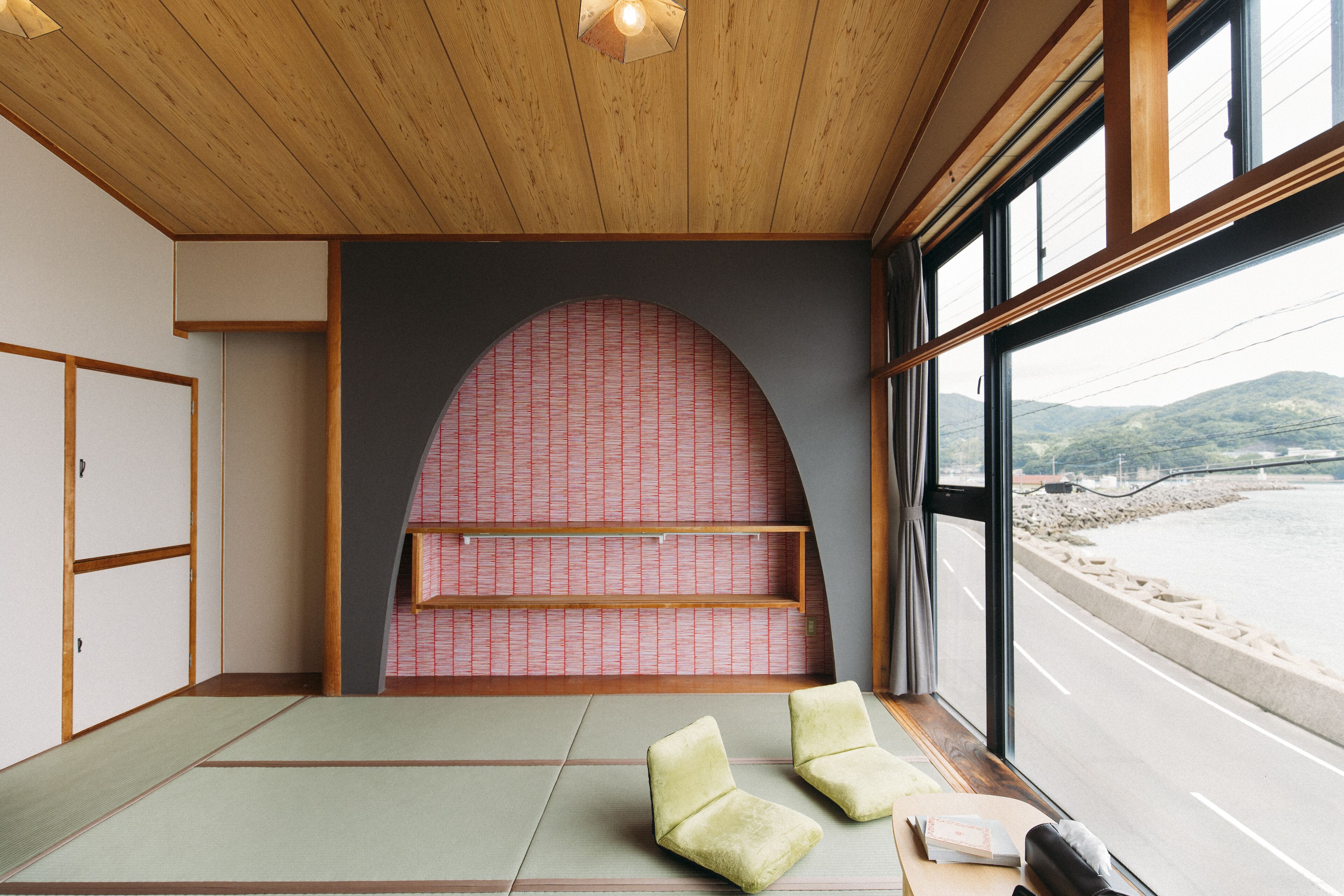 A traditional Japanese room with tatami flooring, a low wooden ceiling, and a view of a beach through large windows.