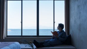 Une personne assise près d’une grande fenêtre, avec vue sur la mer.
