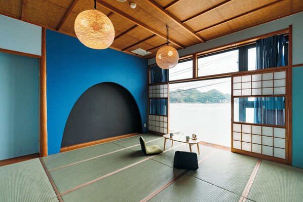 Une pièce de style japonais traditionnel, avec un sol recouvert de tatamis, une petite table basse avec un coussin, et une vue sur un plan d’eau à travers des panneaux coulissants en papier.