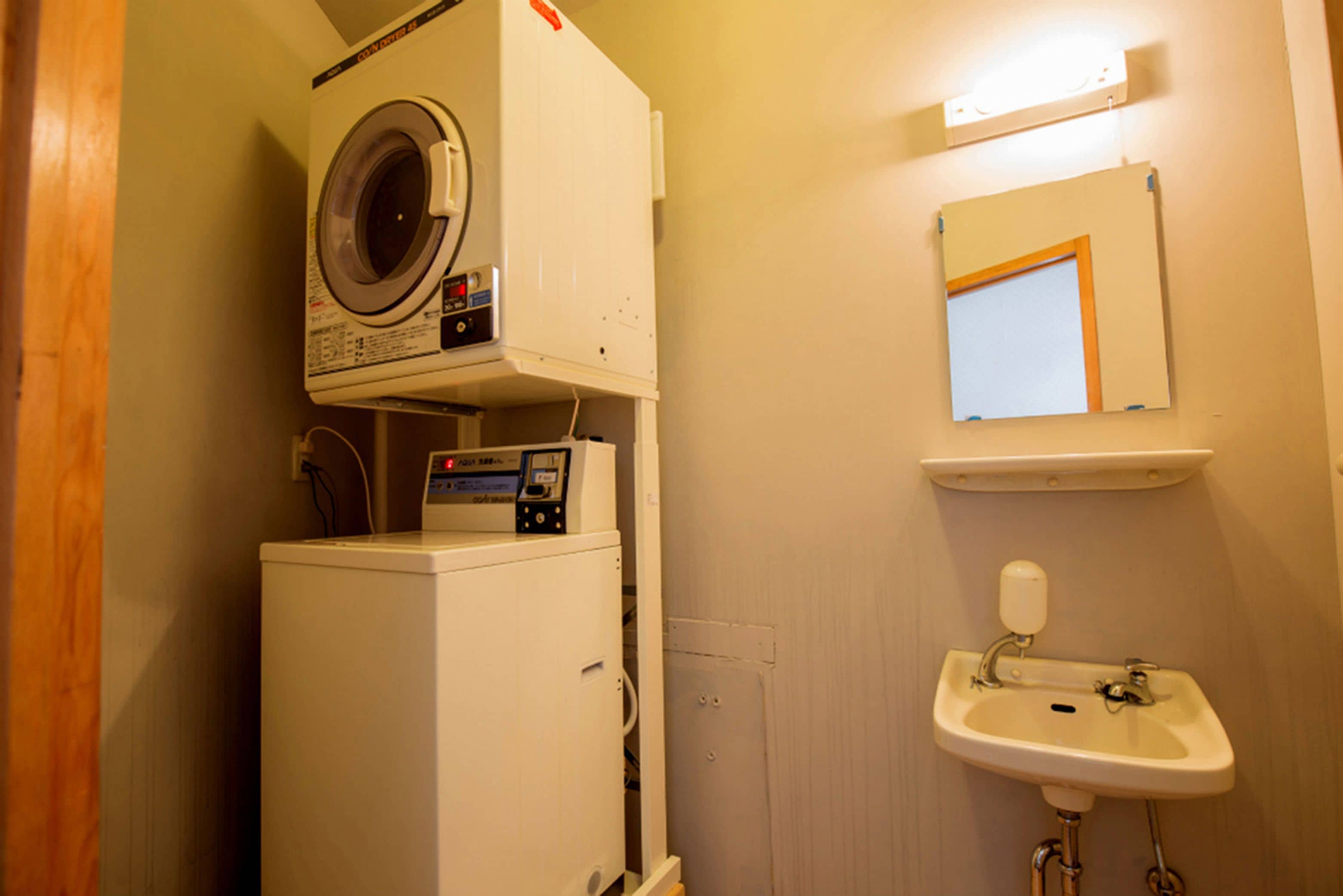 A compact bathroom with a washing machine, a sink, and a mirror.