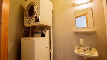 A compact bathroom with a washing machine, a sink, and a mirror.
