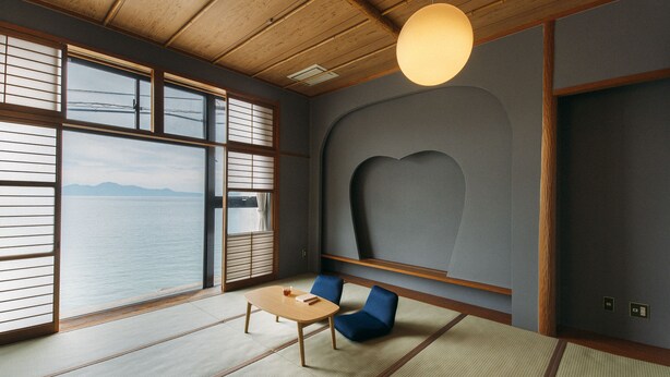 Een traditionele Japanse kamer met tatami vloeren, een lage tafel, blauwe stoelen en uitzicht op zee.