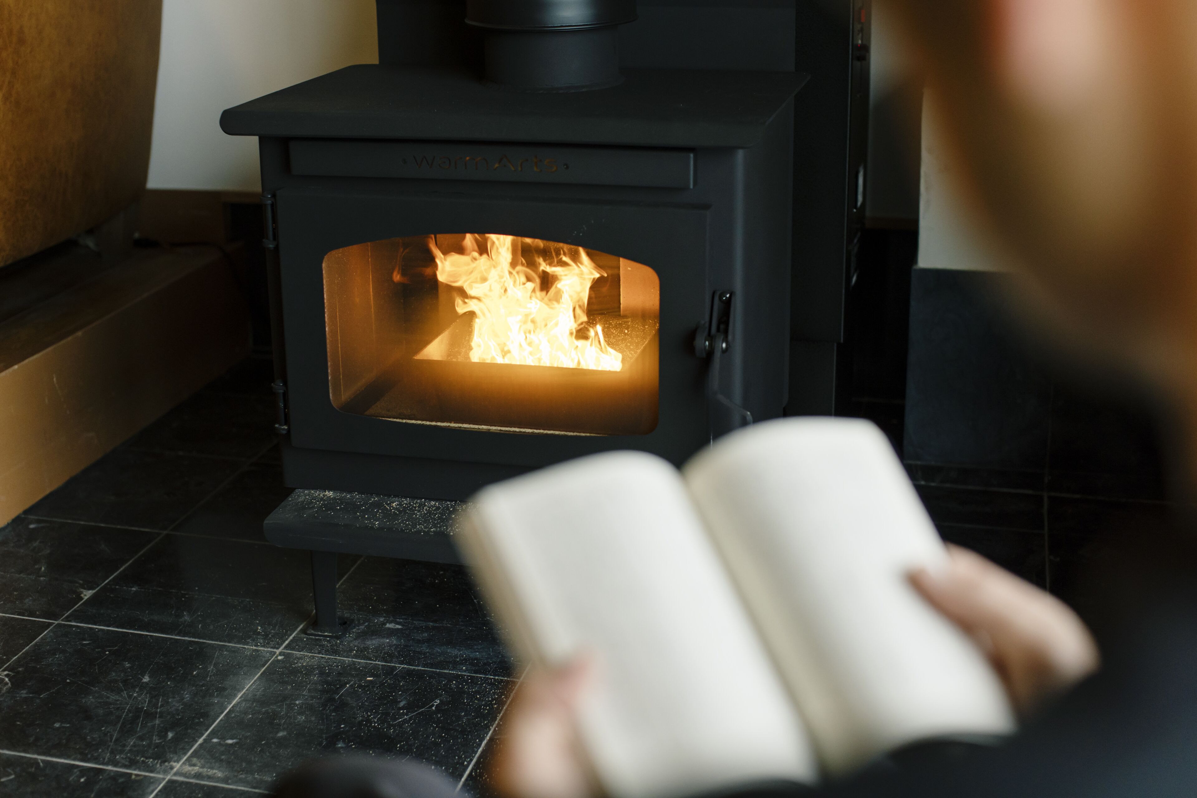En person som sitter och läser en bok framför en vedeldad kamin.