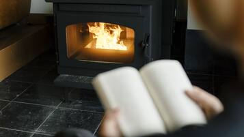 En person som sitter och läser en bok framför en vedeldad kamin.