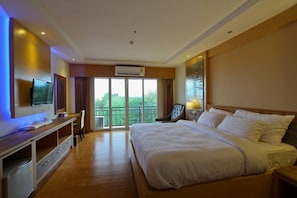 Habitación de hotel con una cama grande, un televisor montado en la pared, un escritorio con una silla y un balcón con vistas a zonas verdes.