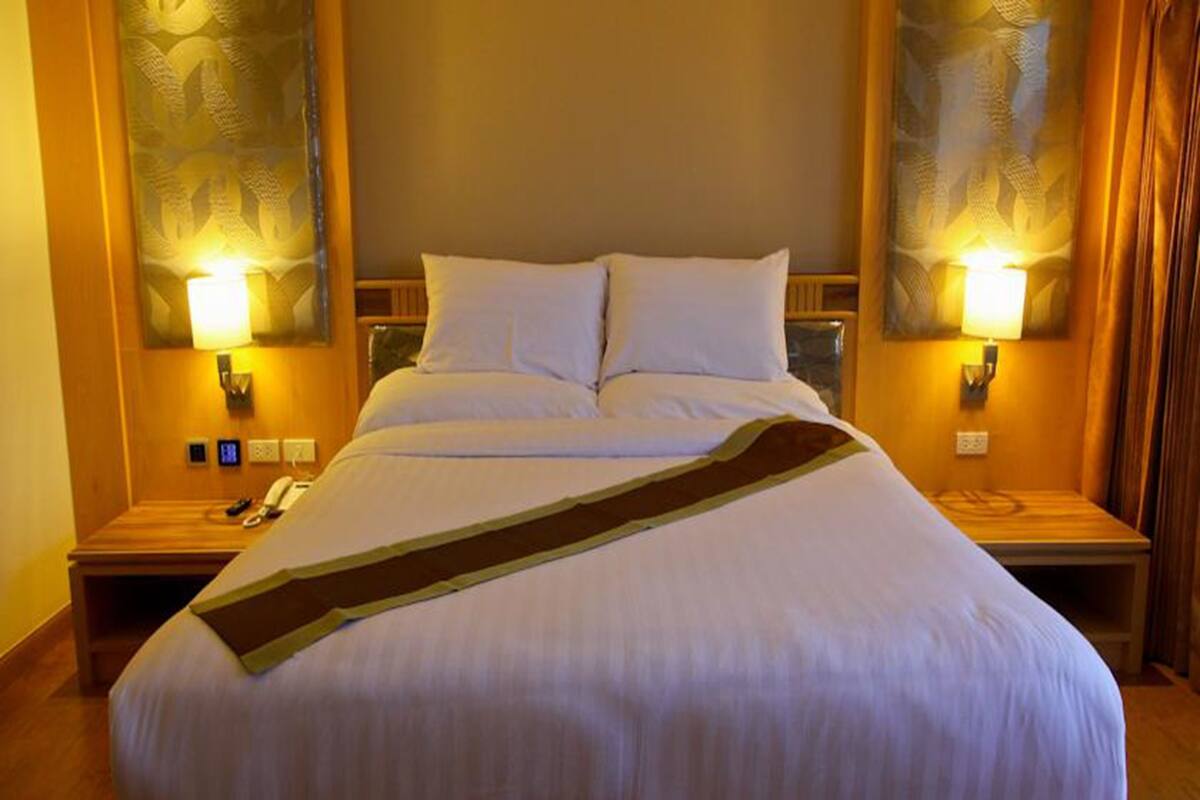 Une chambre d’hôtel avec un grand lit, deux tables de chevet et des lampes fixées au mur.