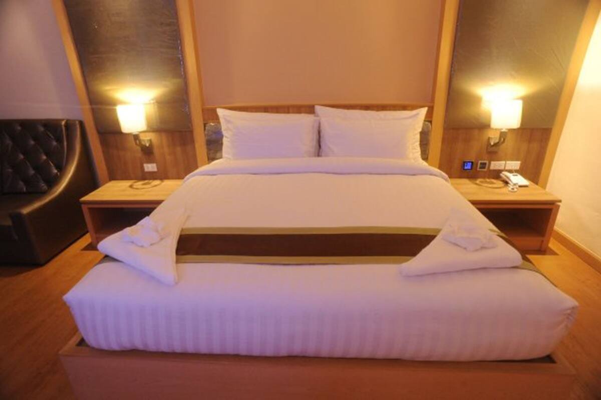 Un lit bien fait, avec du linge de lit blanc, deux tables de chevet avec des lampes et une tête de lit en bois.