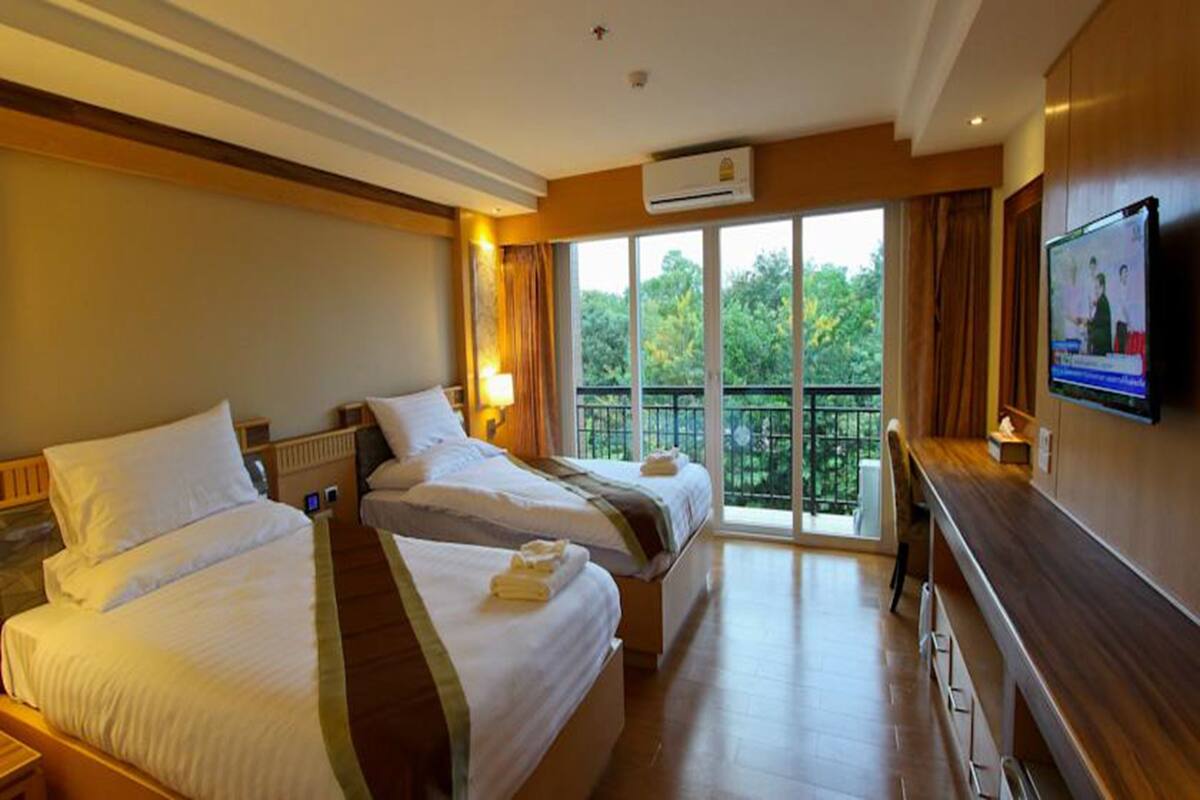 Une chambre d’hôtel avec deux lits, une télévision et un balcon donnant sur la forêt.