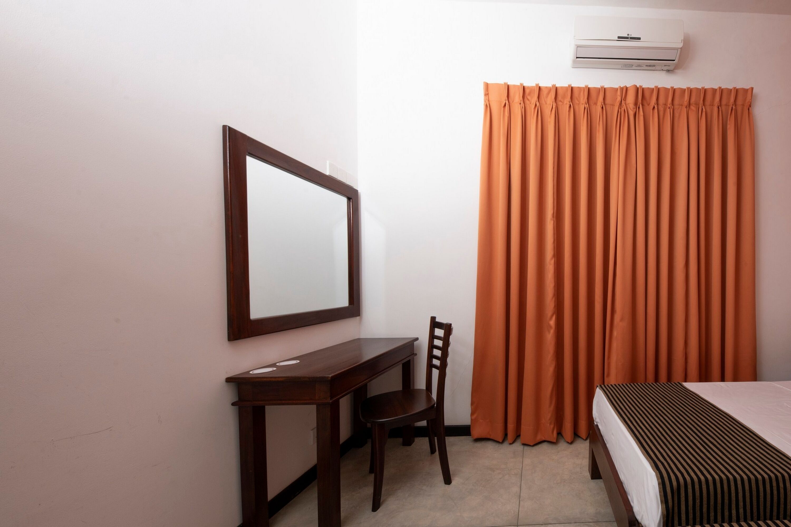 Une chambre d’hôtel avec un bureau en bois, une chaise, un lit recouvert d’une courtepointe à rayures et des rideaux orange.