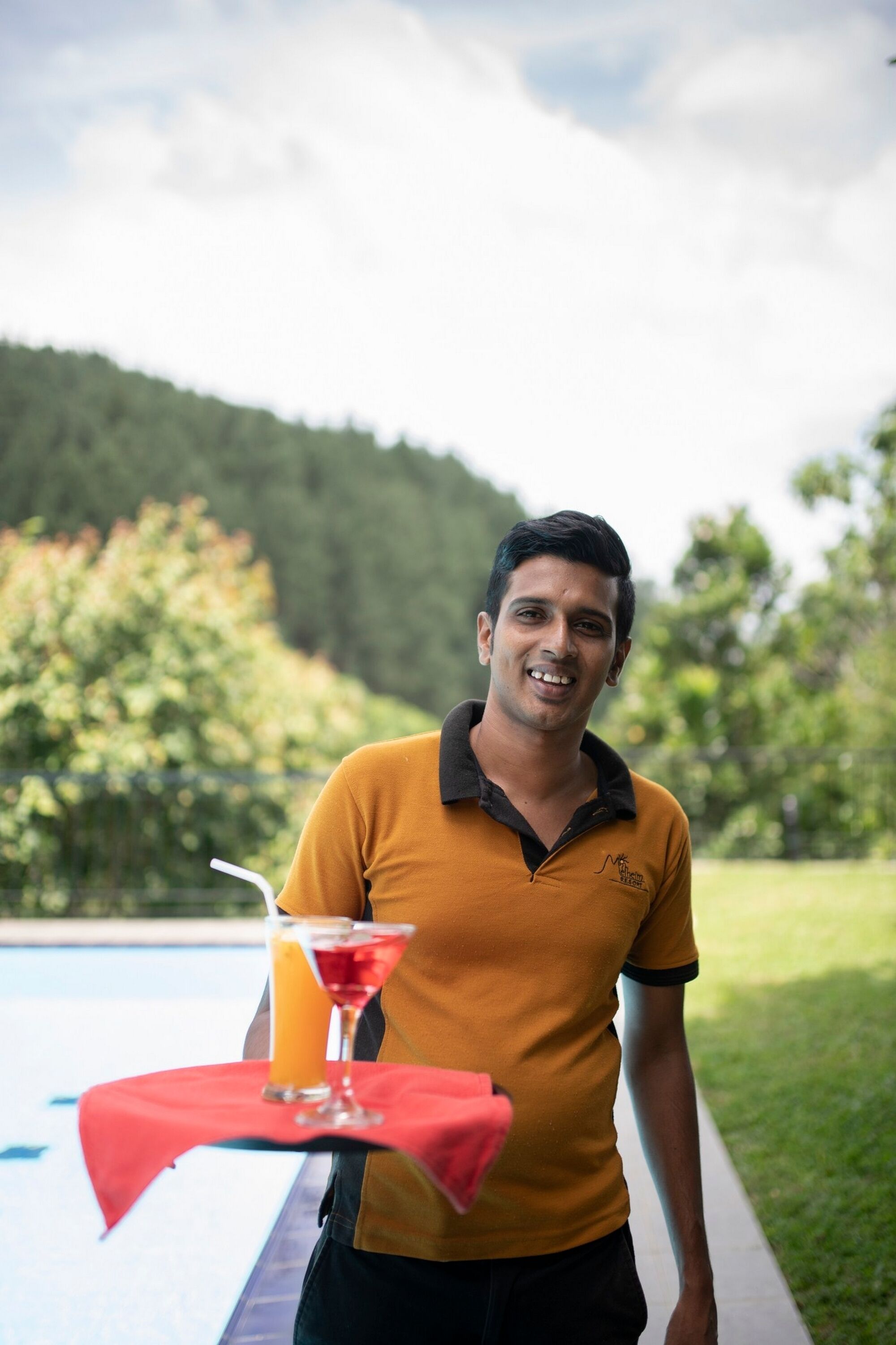 Una persona de pie junto a una piscina con una bebida sobre un mantel rojo.